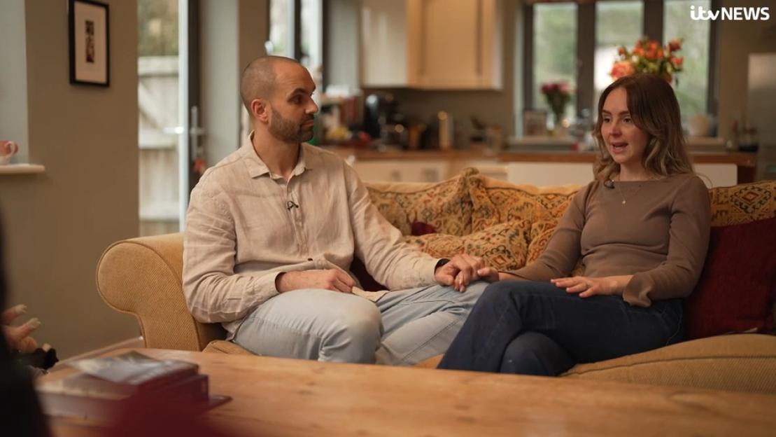 Gus and Emily Forrester holding hands while seated on a sofa.