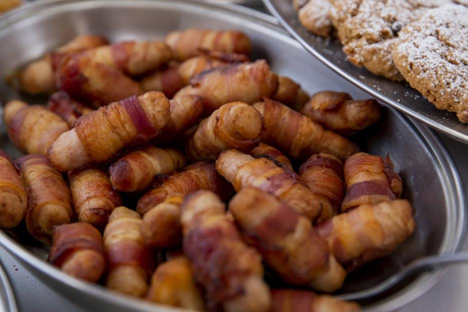 Pigs in blankets in a metal tray, with cookies in the background.