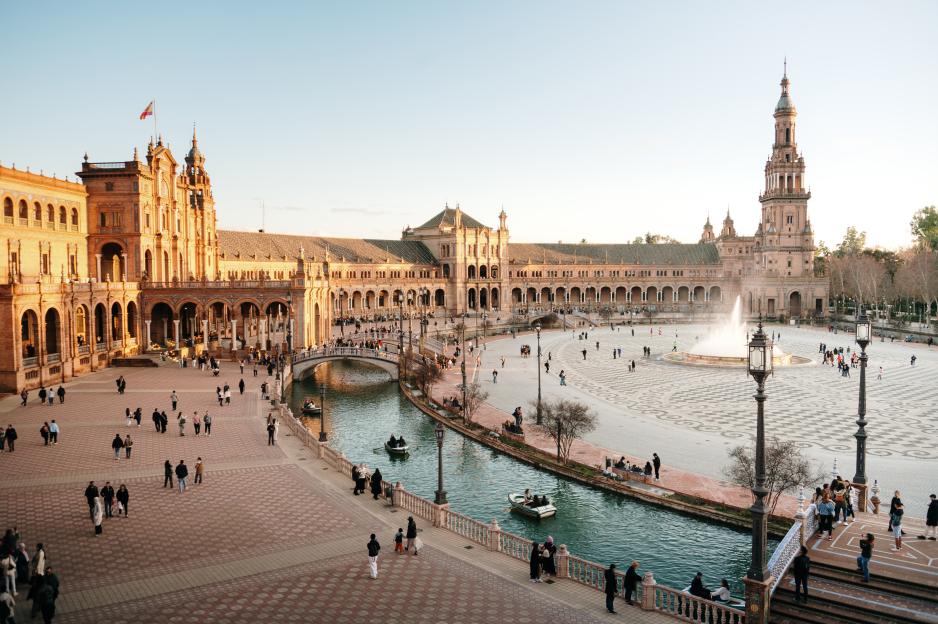 Plaza de España in Seville, Spain, with a canal, boats, and people.