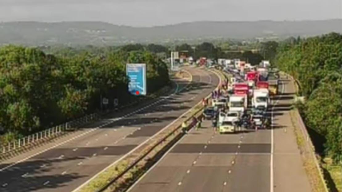 Heavy traffic on the M5 motorway, with numerous trucks and cars stopped in one direction.