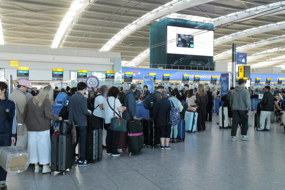 Passengers and their luggage queue at check-in desks at Heathrow Airport.