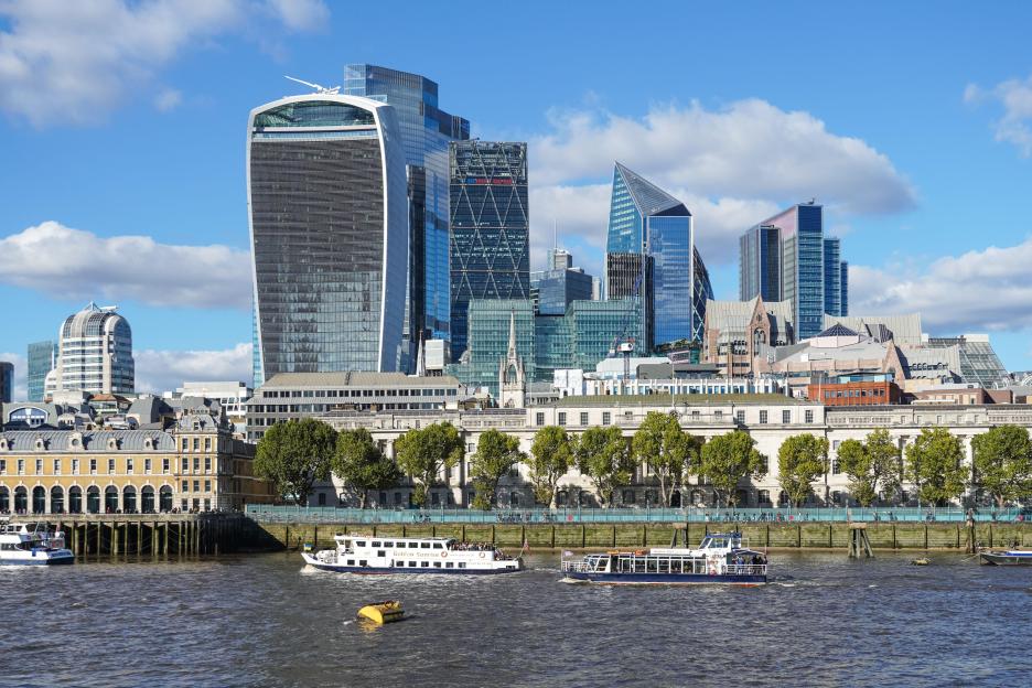 The London cityscape with skyscrapers, traditional buildings, trees, and boats on the River Thames.
