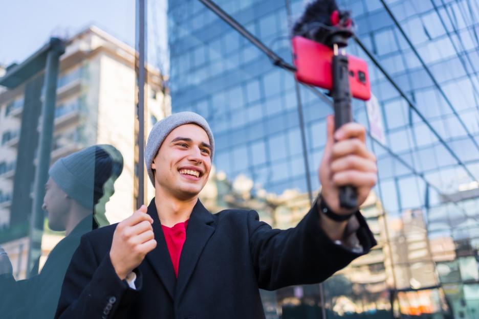 Young man vlogging with a smartphone and external microphone.