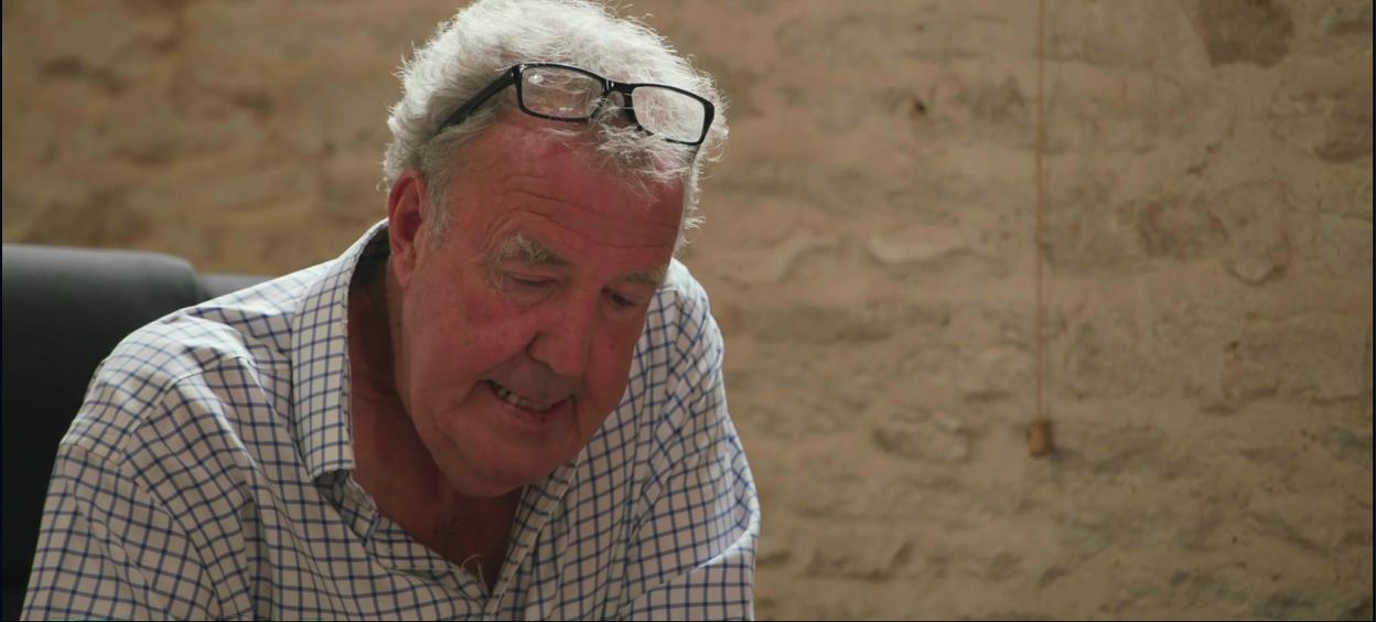 Jeremy Clarkson, wearing a checked shirt and glasses perched on his head, looking down.