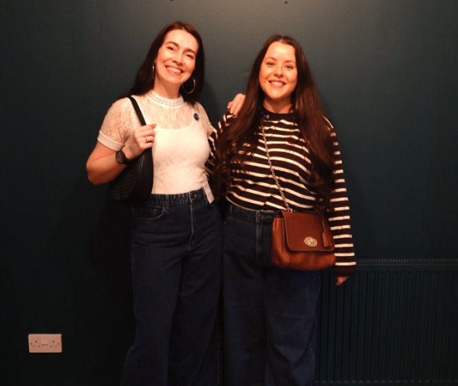 Two women smiling in dark blue jeans and tops.