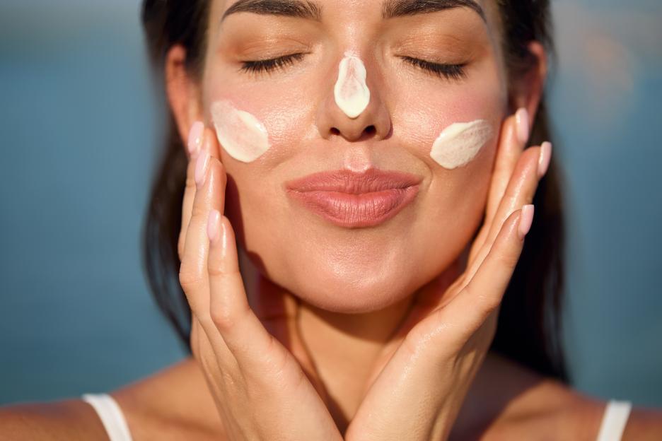 A woman applying sunscreen to her face, with streaks visible on her nose and cheeks.