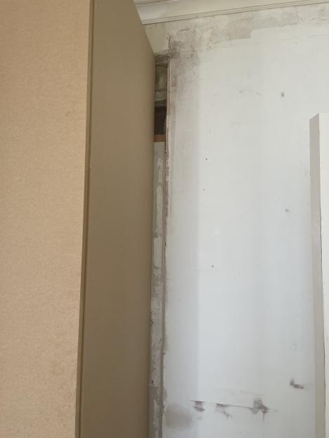 A gap between a light brown panel and a white wall, revealing exposed brick and plasterwork.