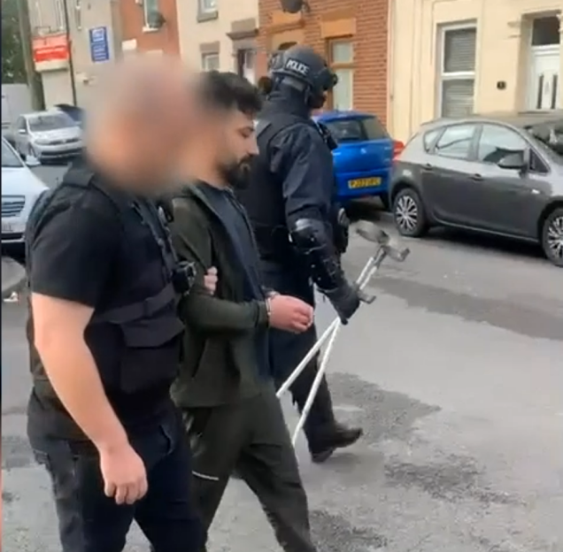 Amanj Hasan Zada, handcuffed, is escorted by two officers on a street.