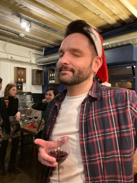Steve Roe wearing a Santa hat and plaid shirt, holding a glass of red wine at a party.