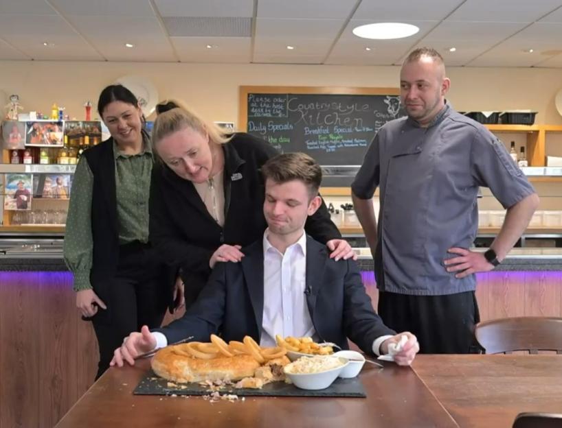 A man sitting in front of a huge pie and fries, with a woman and two men standing behind him.