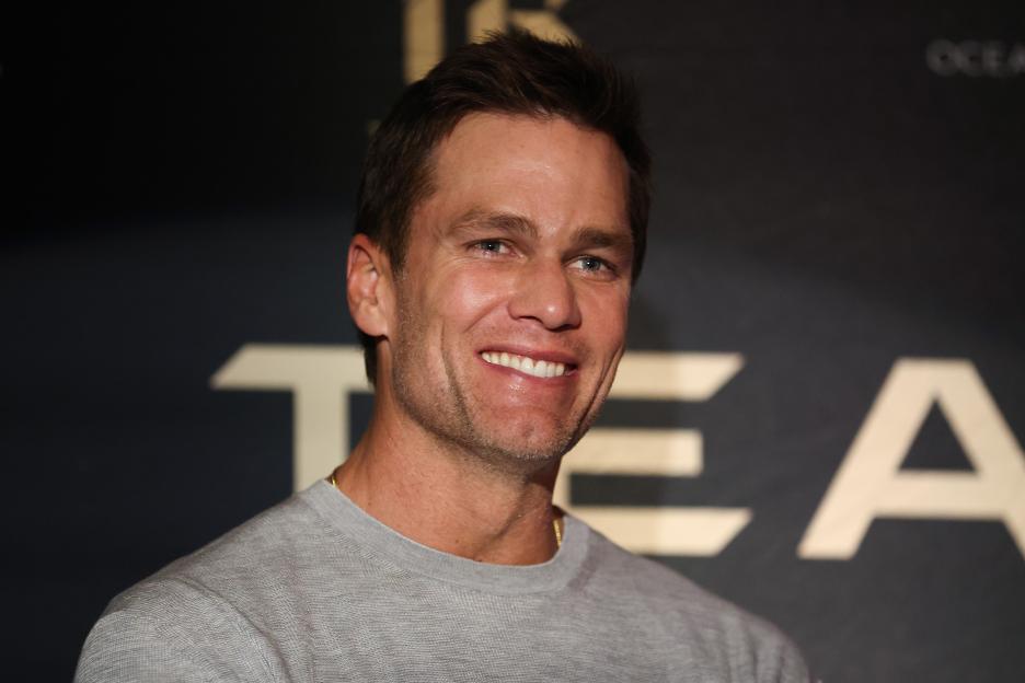 Tom Brady smiling in front of a dark background with gold lettering.