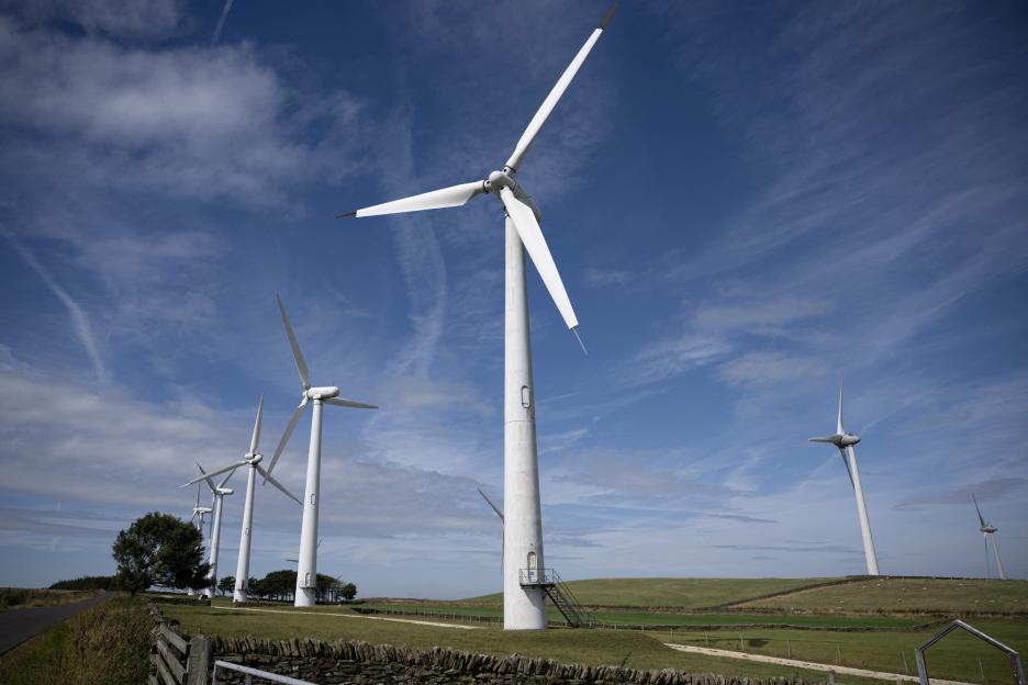 Wind turbines on a green field under a blue sky with scattered clouds.