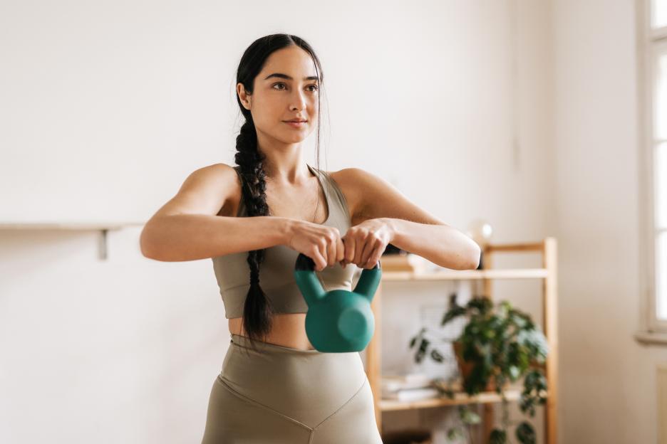 A sporty woman exercising with a green kettlebell at home.