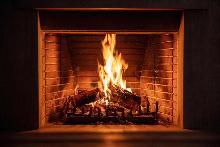 A fireplace with bright orange and yellow flames burning logs against a brick background.
