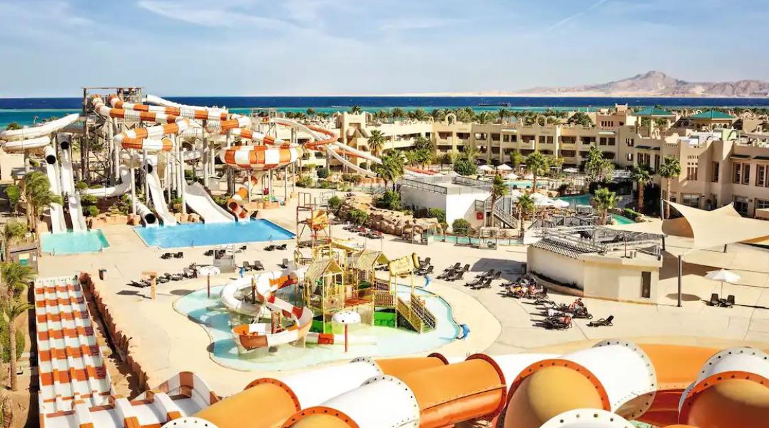 A large water park with multiple slides and pools at a resort next to the ocean.