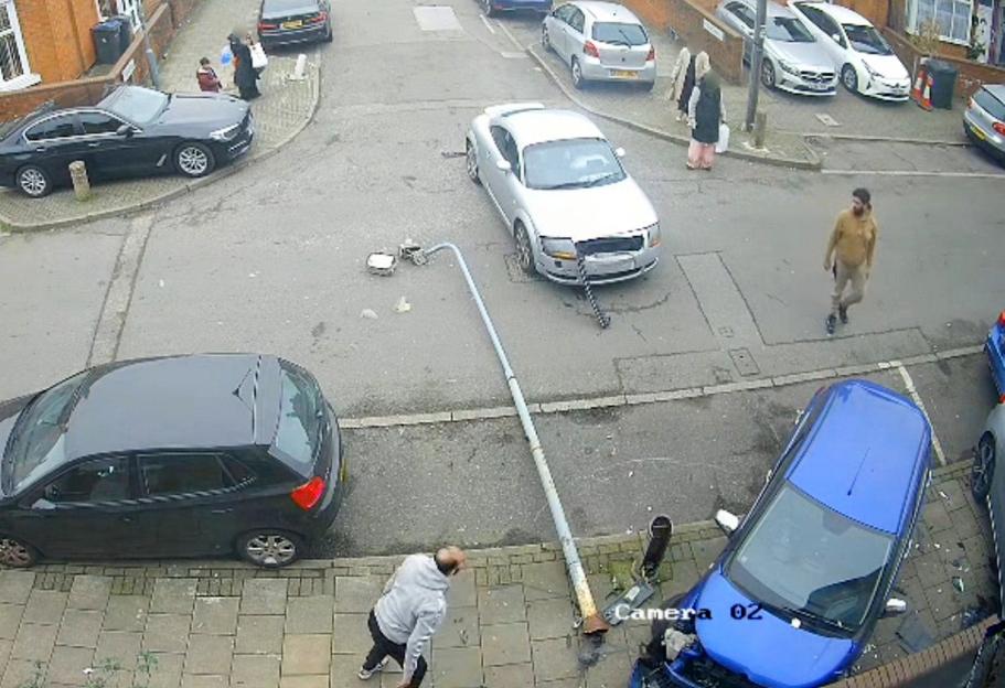 Overhead view of a street after a car crash, showing debris from a broken lamppost, a blue car with front-end damage, and a silver car with a broken front bumper.