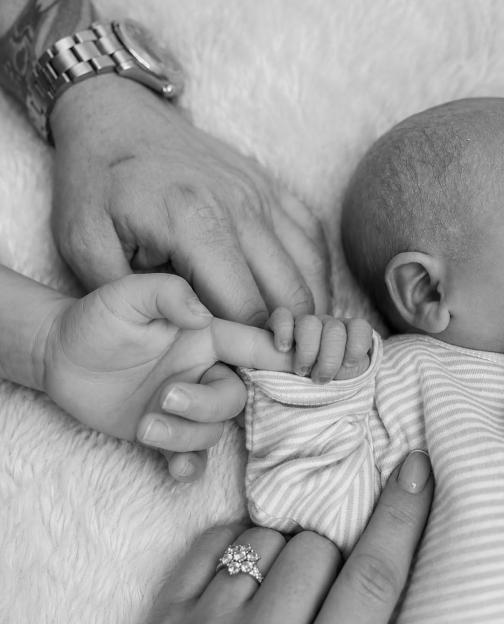 Black and white image of an adult's hand, a baby's hand holding an adult's finger, and another adult hand with a ring.