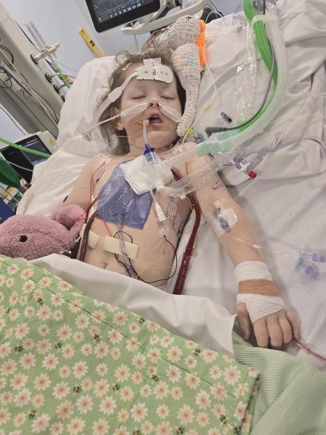 A mother comforts her toddler daughter in a hospital bed, surrounded by medical equipment.