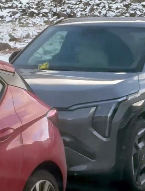 A parking ticket on the windshield of a grey SUV parked bumper to bumper with a red car on a snowy road.