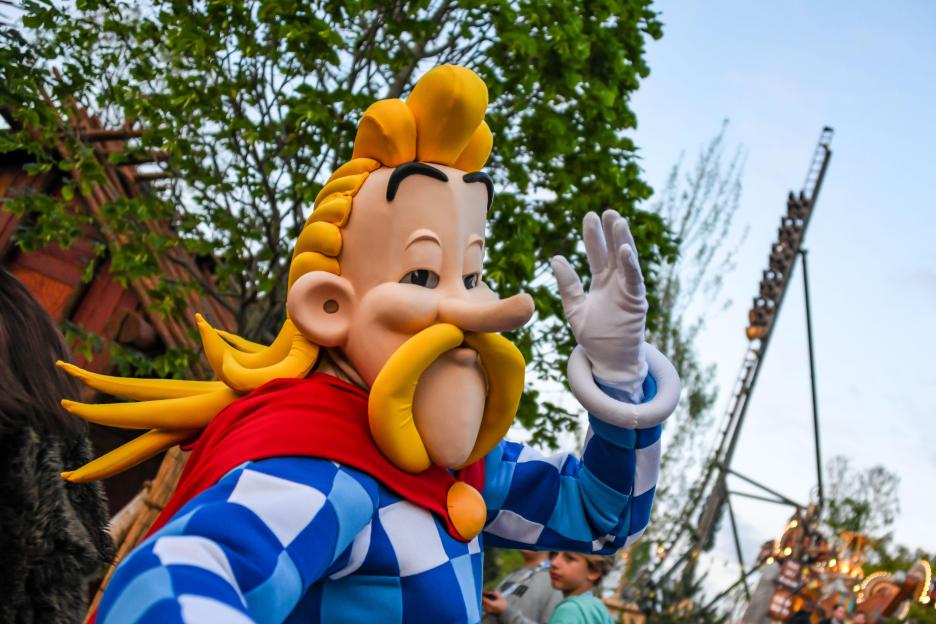 Costumed character in blue and white checks with a red cape and yellow hair at the Toutatis Festival area at Parc Astérix.