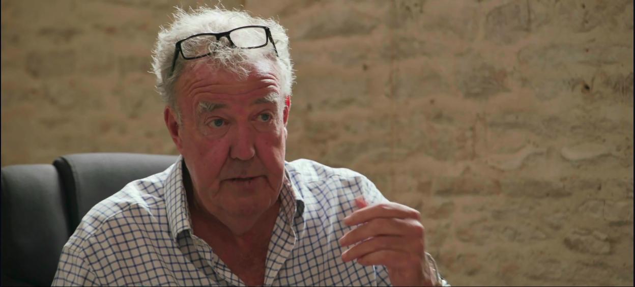 Jeremy Clarkson in a blue and white checkered shirt, with glasses resting on his head, shares cancer diagnosis with Kaleb and Charlie.