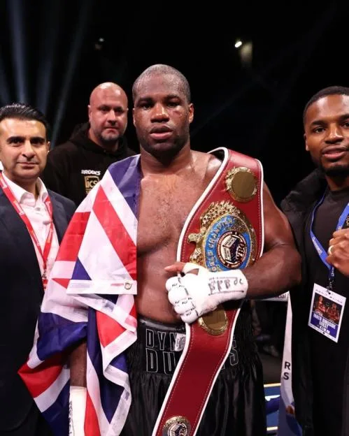 Daniel Dubois poses with his championship belt and a British flag, surrounded by his team.