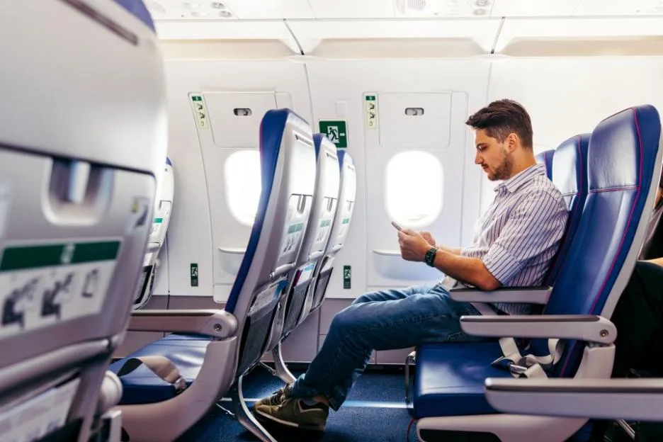 Man in airplane seat uses a smartphone.