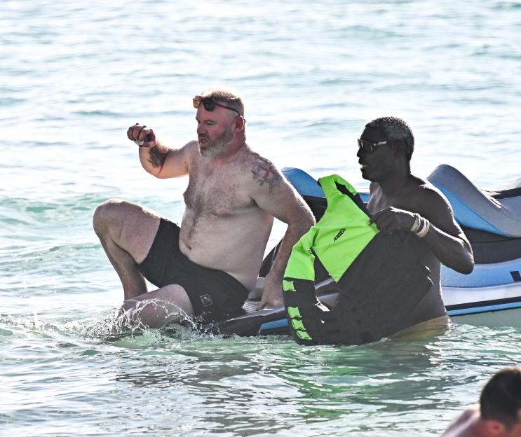 Wayne Rooney and a man with a bright green life vest on a jet ski in the ocean.