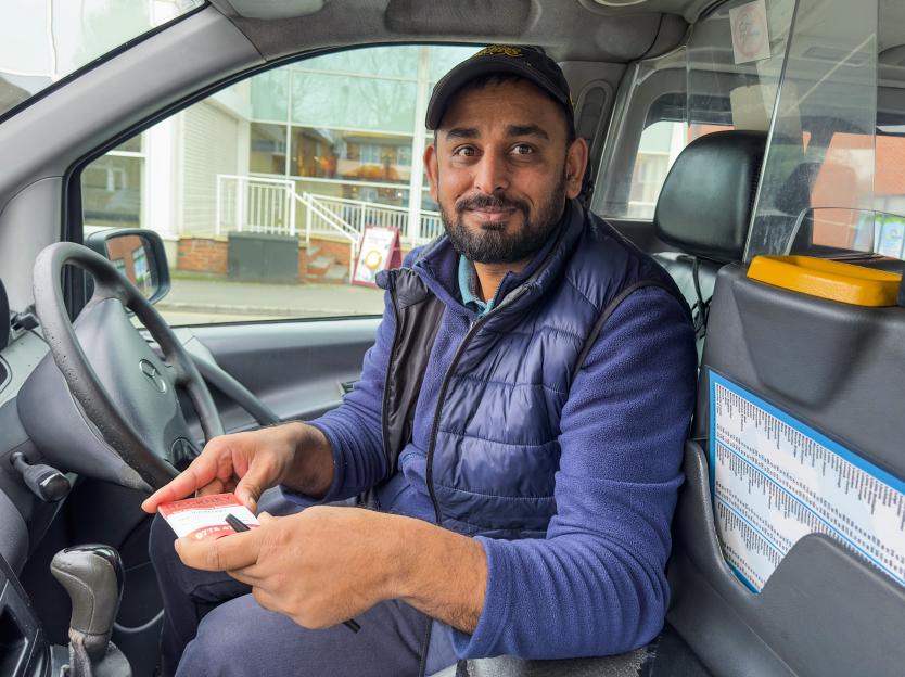 Taxi driver Raja Ahmed sits in his taxi holding a receipt pad.