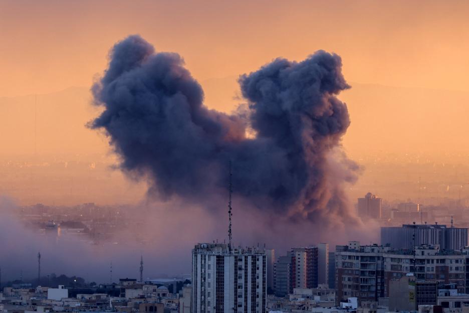 A plume of smoke rising from a strike in Tehran, above a cityscape at sunset.