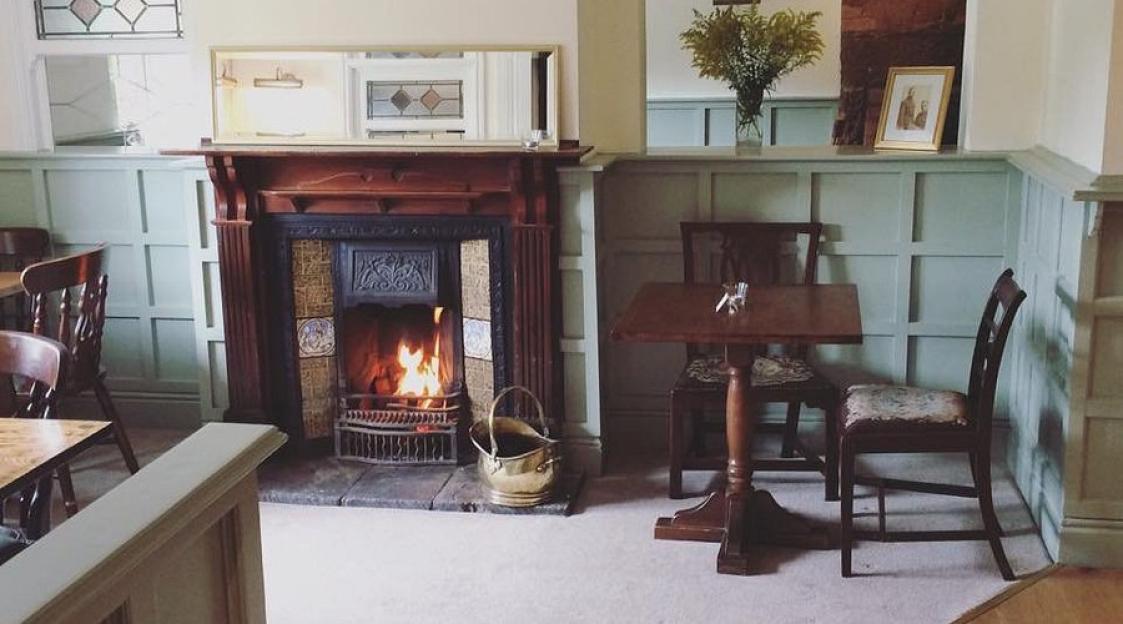 A cozy room with a lit fireplace, two chairs, and a small table.