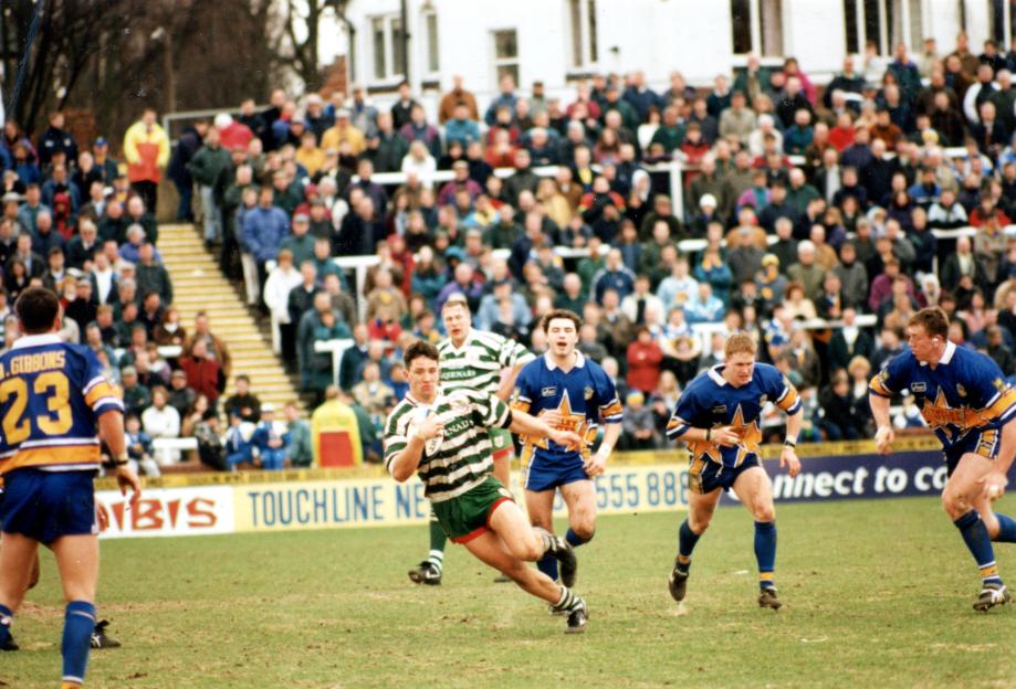 Leeds and Warrington rugby players in action on the field with spectators in the background.