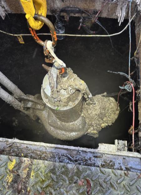 A sewage pump covered in a thick layer of fat, wet wipes, and condoms, being lifted by a large hook.