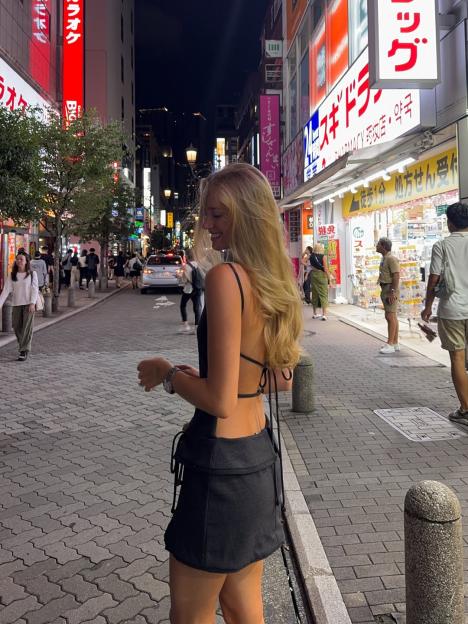 Desire Inglander smiling in a street with neon signs in Japanese.