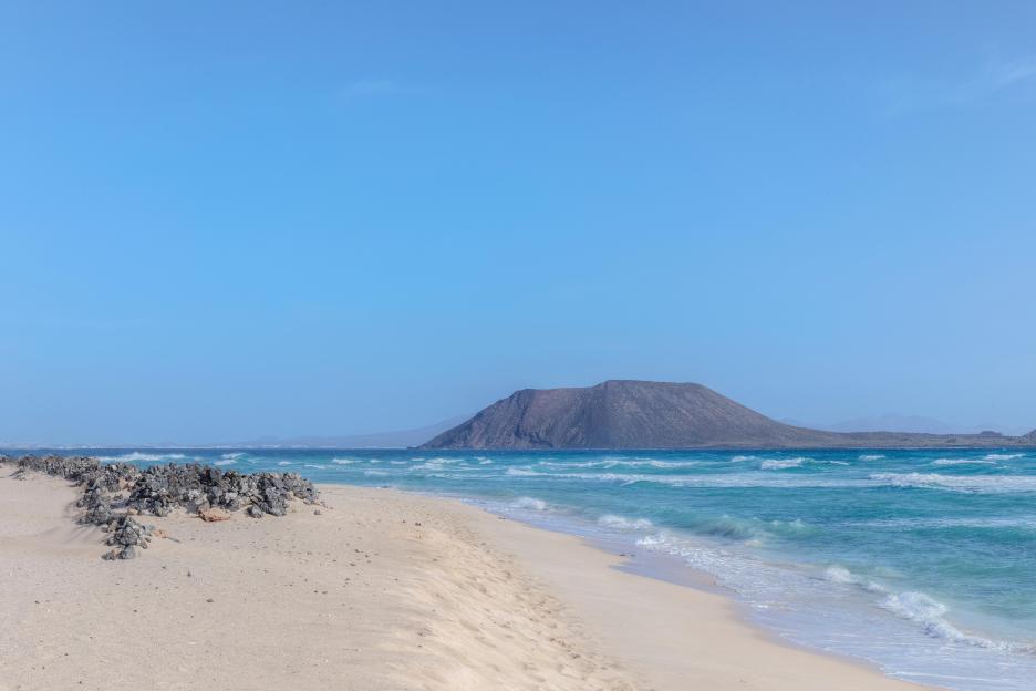 Corralejo Natural Park beach with turquoise waves and a large, dark mountain in the background.