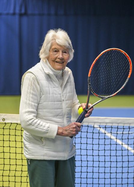 Shirley Critchley, a 93-year-old woman, stands on a tennis court holding a tennis racket and ball.