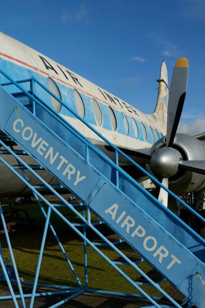 Blue stairs with "COVENTRY AIRPORT" written on them lead up to an old white and blue propeller airplane.