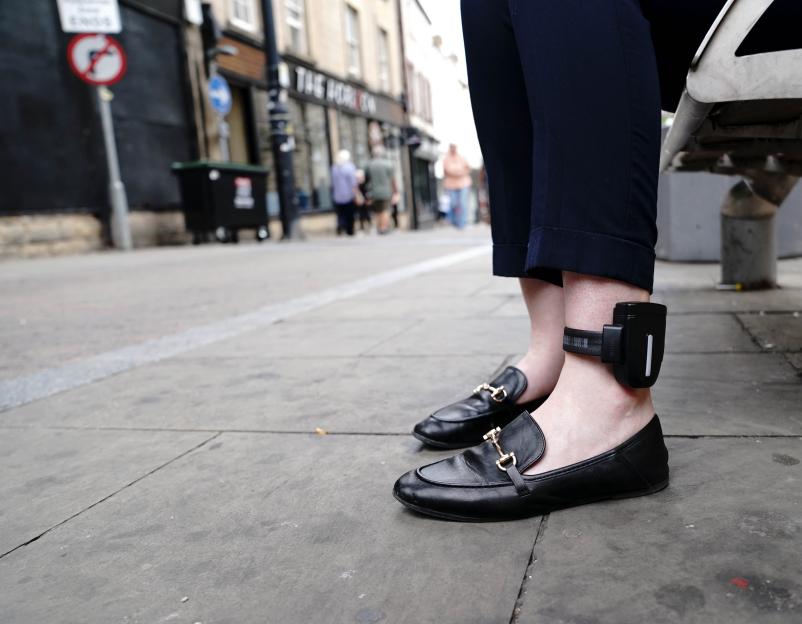 A close-up of a person's lower legs and feet, showing a GPS monitoring tag attached to one ankle.