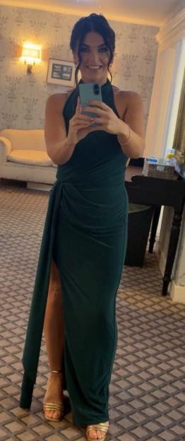 A woman wearing a dark green halter-neck dress with a high slit, taking a mirror selfie.
