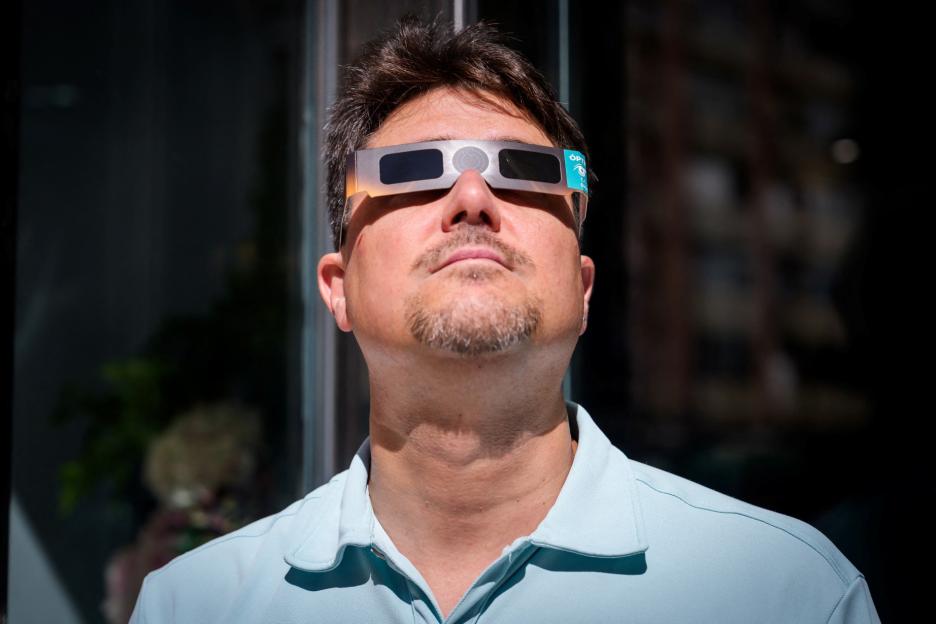 A man wearing solar eclipse glasses looks up.