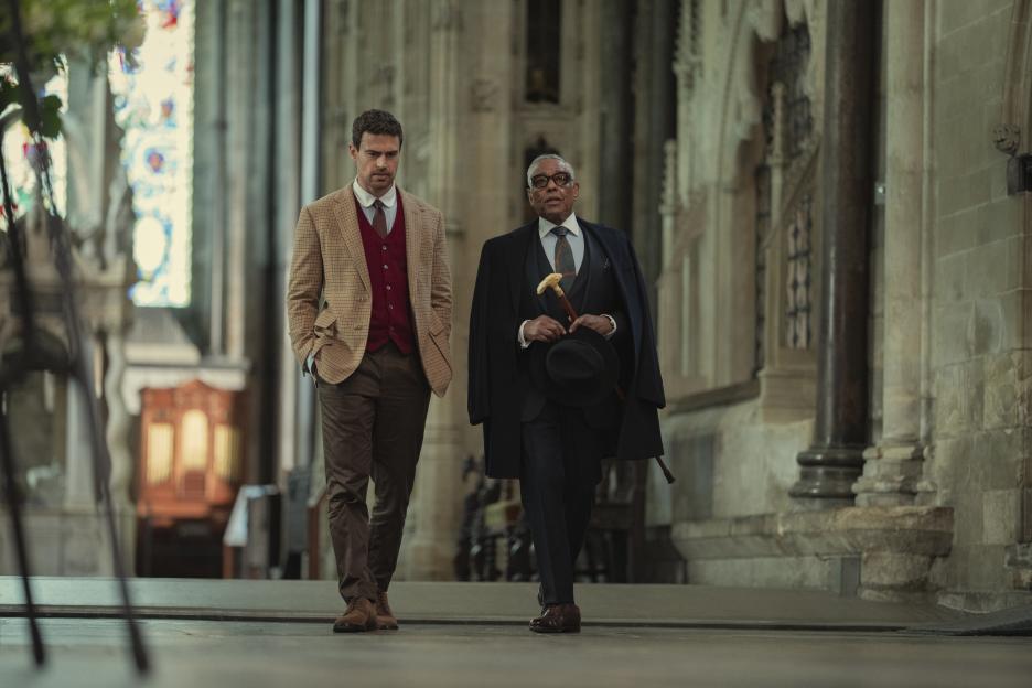 Two men walk down the aisle of a cathedral, the younger man on the left and the older man on the right.