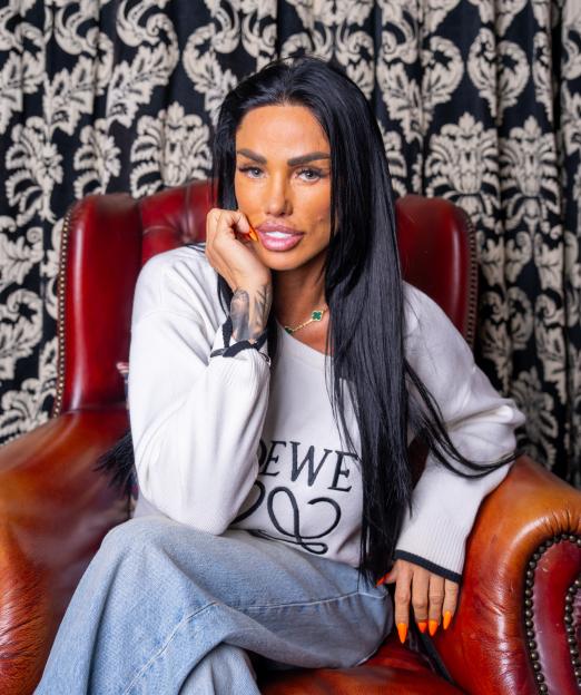 Katie Price seated in a red leather armchair against a black and white patterned curtain.