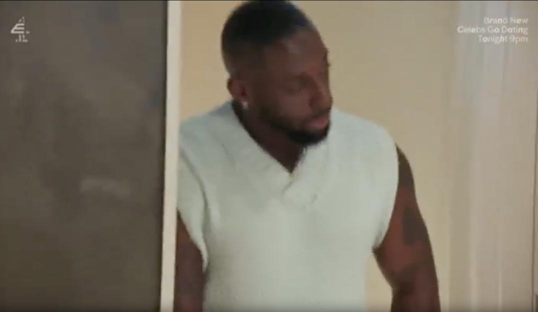 A man with a beard and a light-colored sleeveless sweater looks to the side.