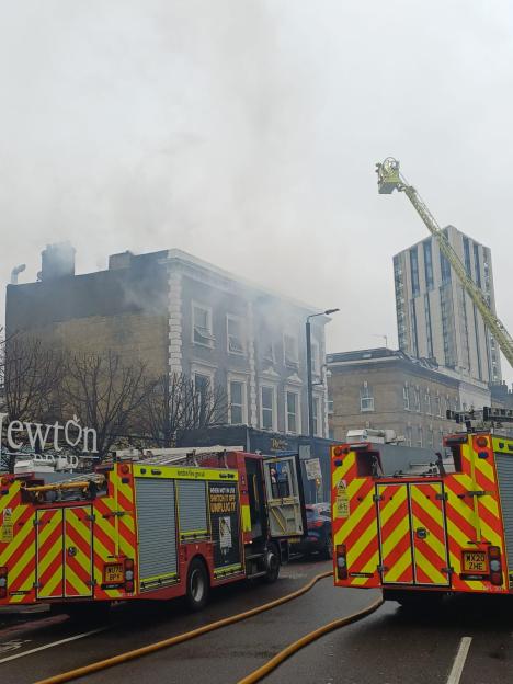 Fire engines and an aerial ladder operating at a fire, with smoke billowing from a building.