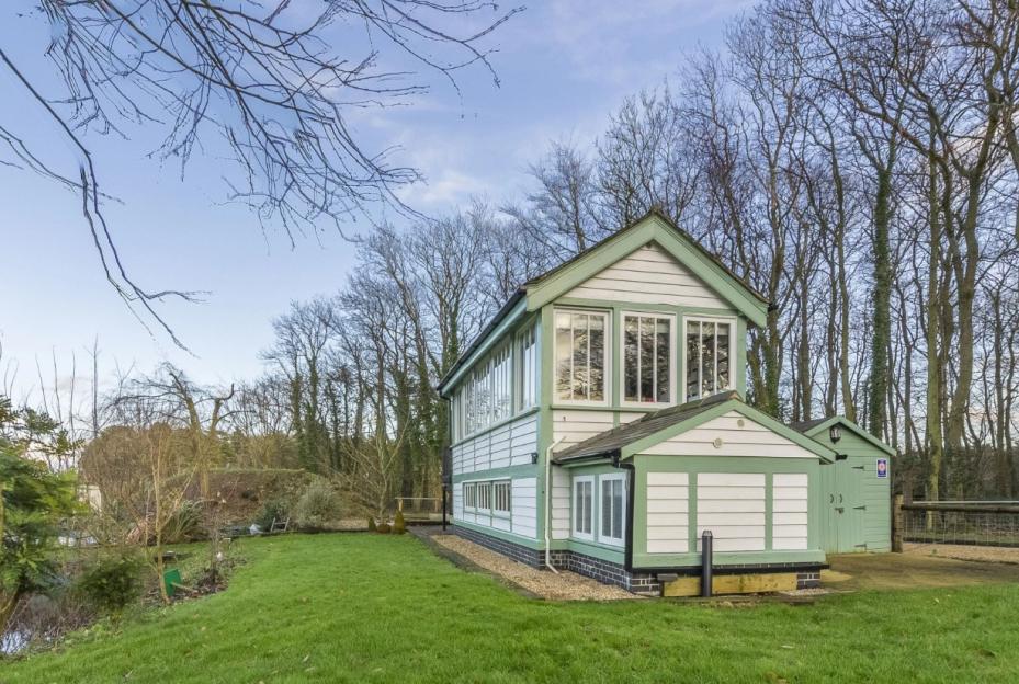 A two-story white and green house with a green shed next to a forest.