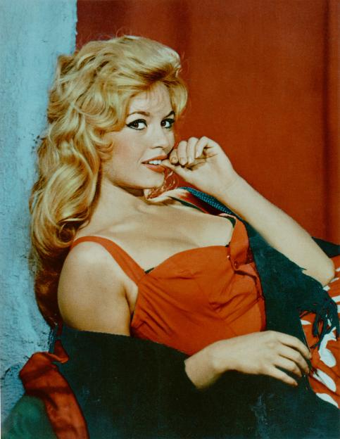 French actress Brigitte Bardot in a red top, biting her finger.