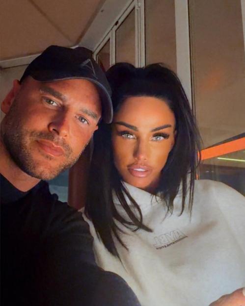 A man in a black cap and a woman with long dark hair, wearing a white hoodie, taking a selfie together.