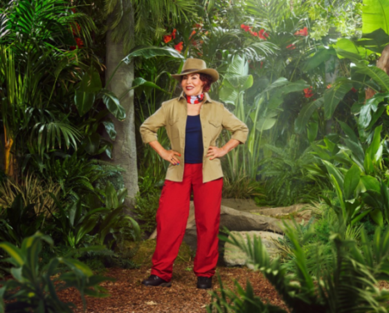 Woman in a safari outfit and hat standing in a jungle setting.