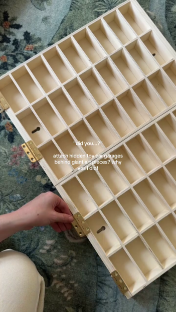 A person attaching a wooden toy car garage to a wall.