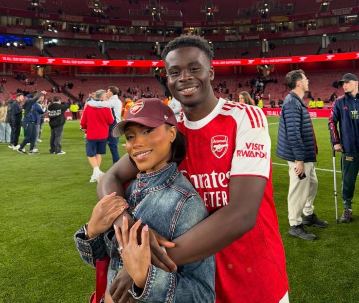Bukayo Saka and Tolami Benson posing on the field of a soccer stadium.